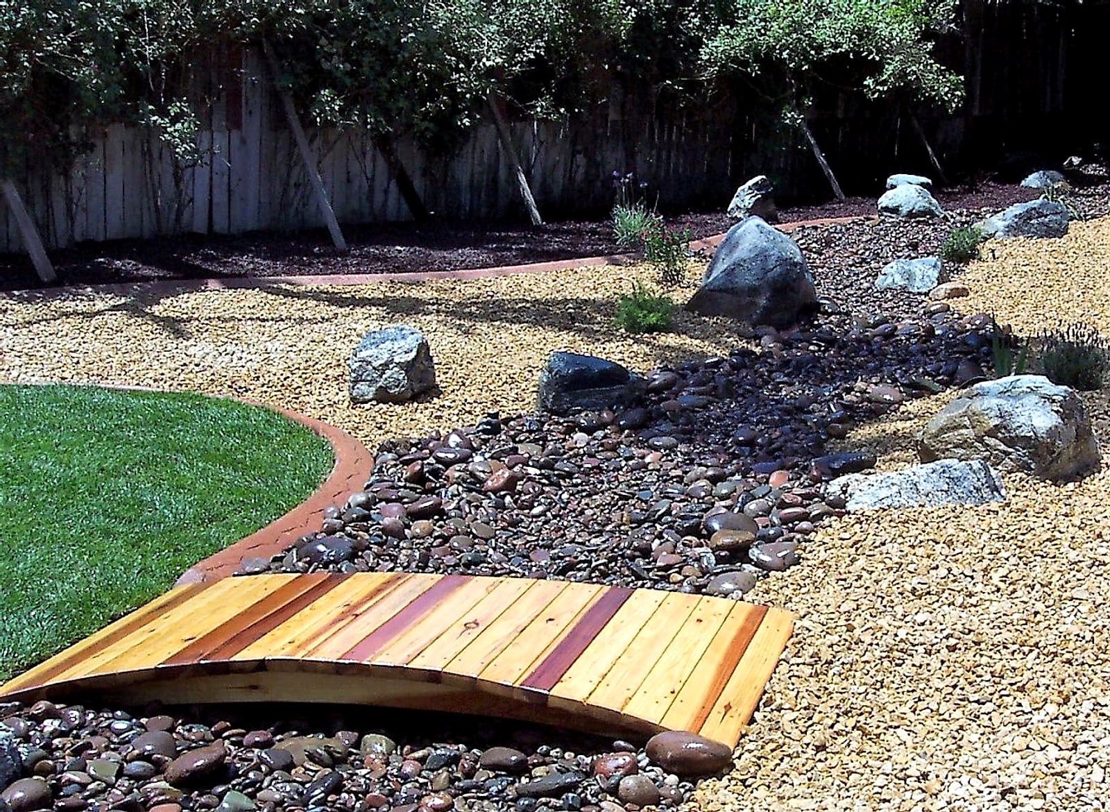 The finished yard: a redwood footbridge over a river rock dry creek, boulders and a curbed lawn