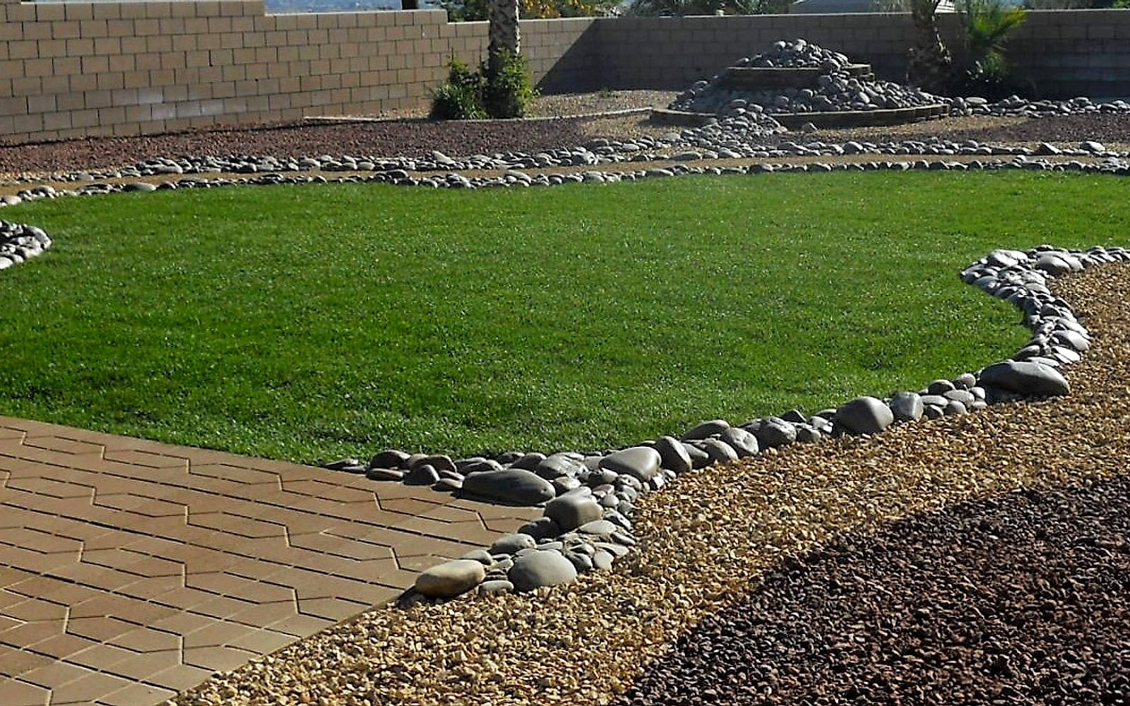 Curved green lawn edged with river cobble next to a paver path