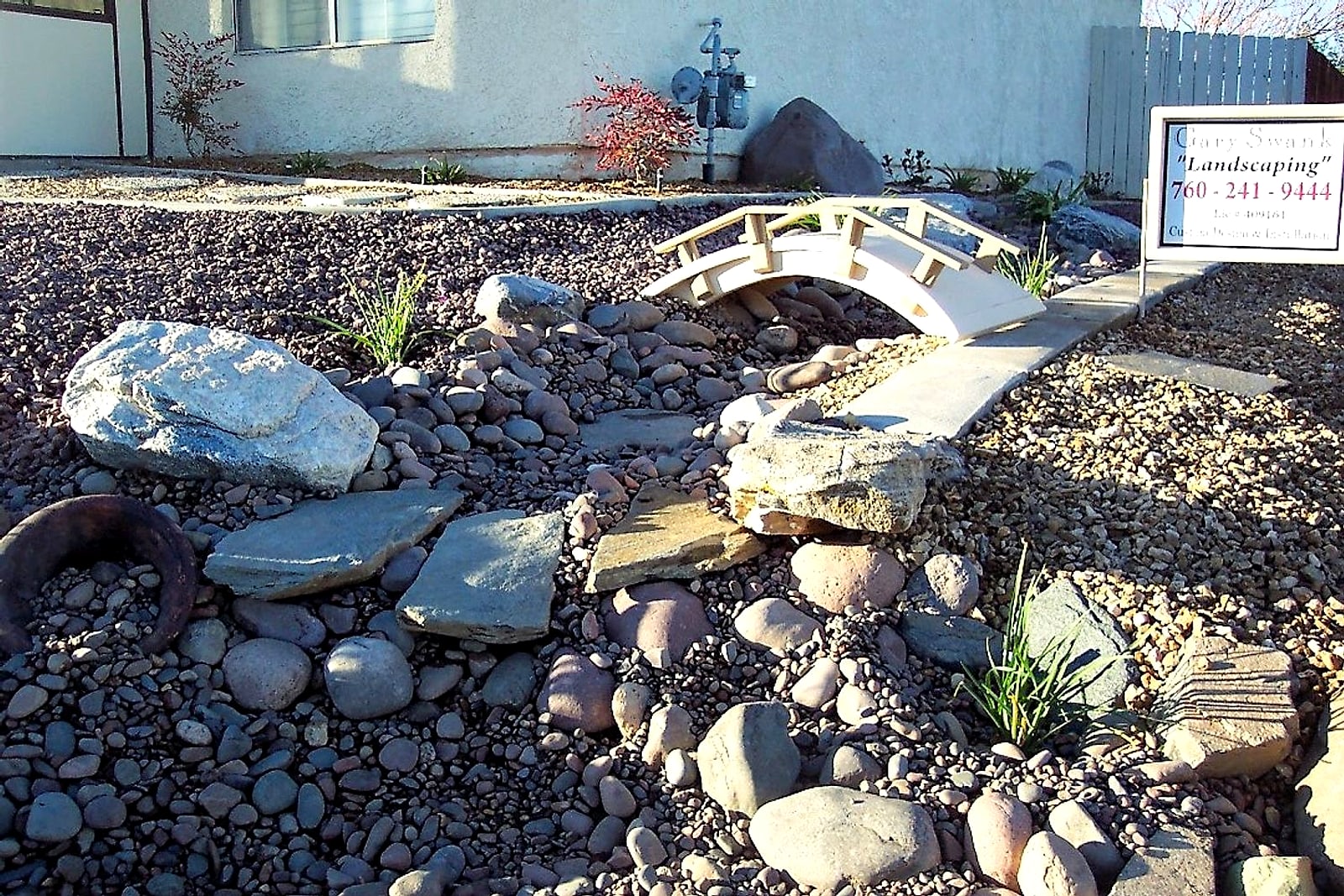 Front yard dry creek bed with a small white bridge and flagstone steps