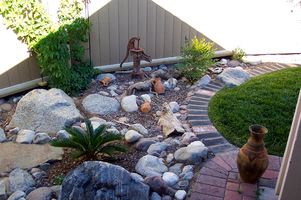 Dry creek bed with an antique pump and a clay pot beside a brick path