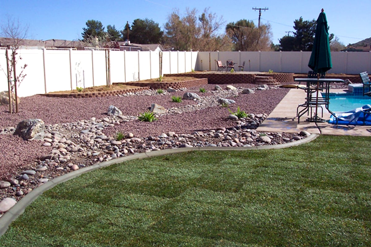 Backyard with a curbed lawn and red rock beds by the pool