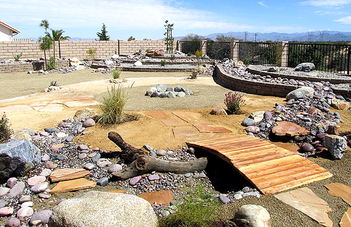 A backyard by Gary with a wooden bridge over a dry creek and flagstone