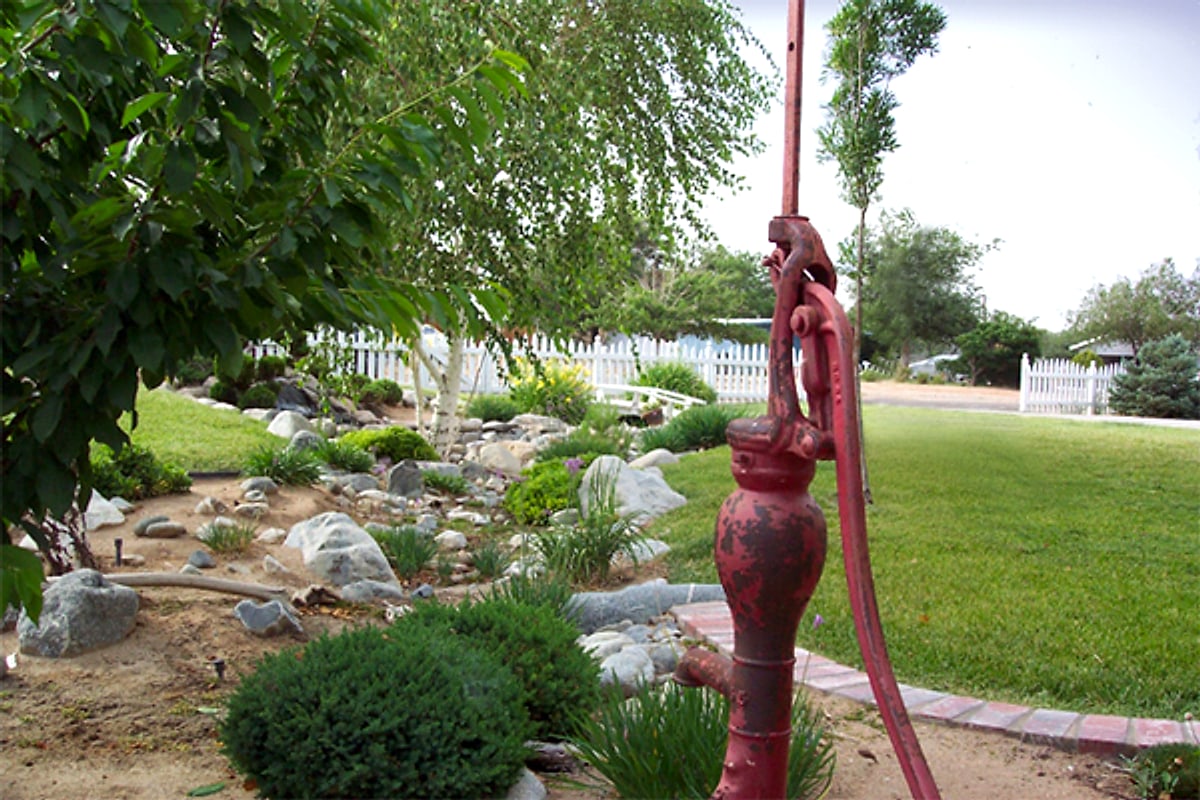 Dry creek bed beside a lawn with an antique red water pump